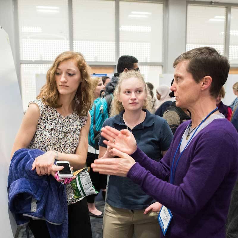female professor talks to female students standing in front of research poster